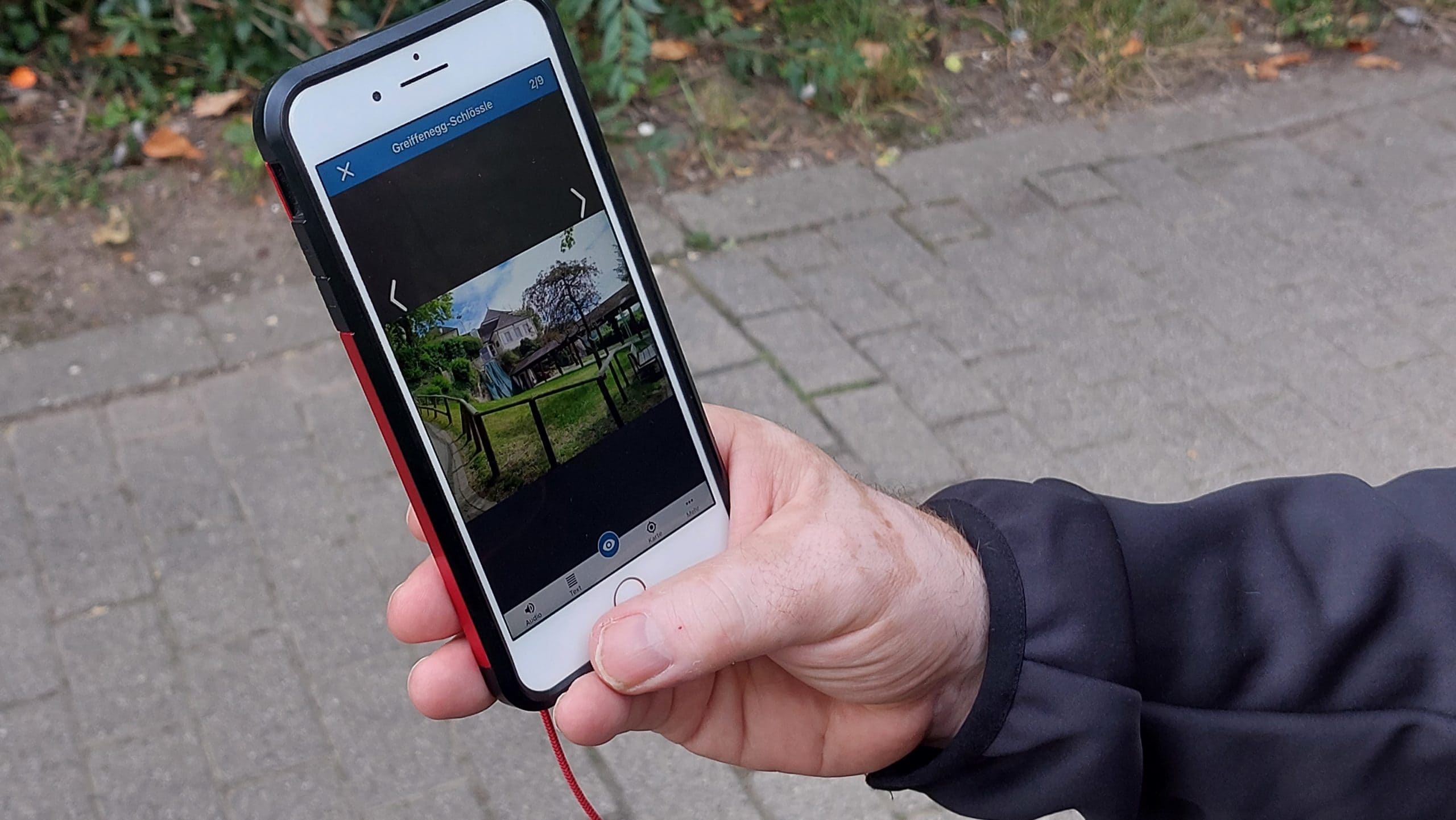 Eine Hand hält ein Smartphone mit einer App für eine Stadtführung Freiburg, die das Greiffenegg-Schlössle als digitales Zielobjekt anzeigt.