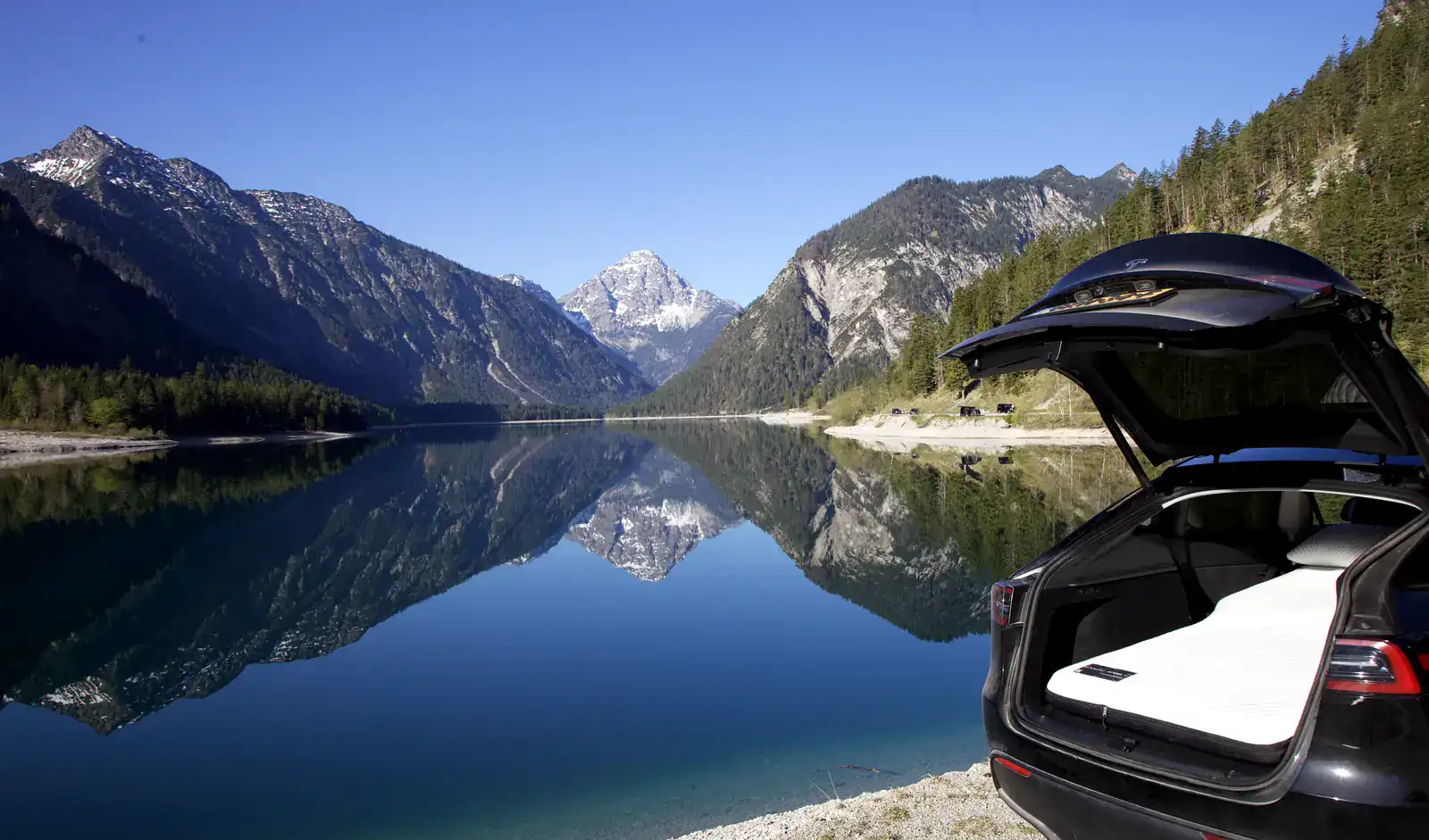 Tesla Model Y met een Snuuzu-matras in de open kofferbak aan een bergmeer