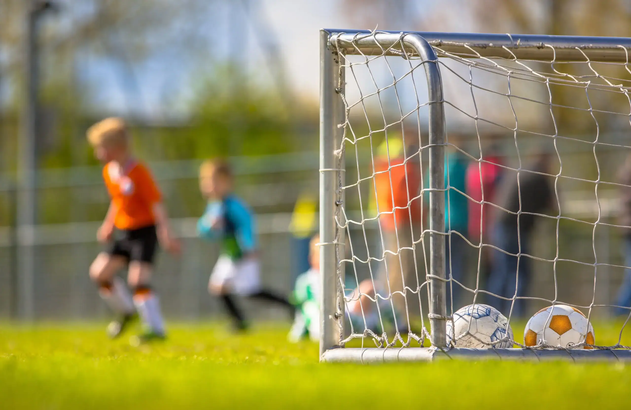 Soccer goal on a community sports field with children playing recreational soccer in the background.