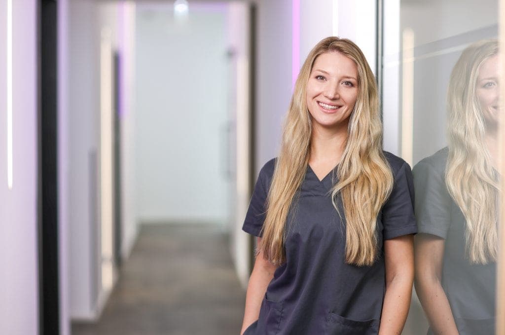 Pflegekraft in Krankenhausuniform vor Klinikflur, lächelnd, professionell, medizinisches Personal, G.
