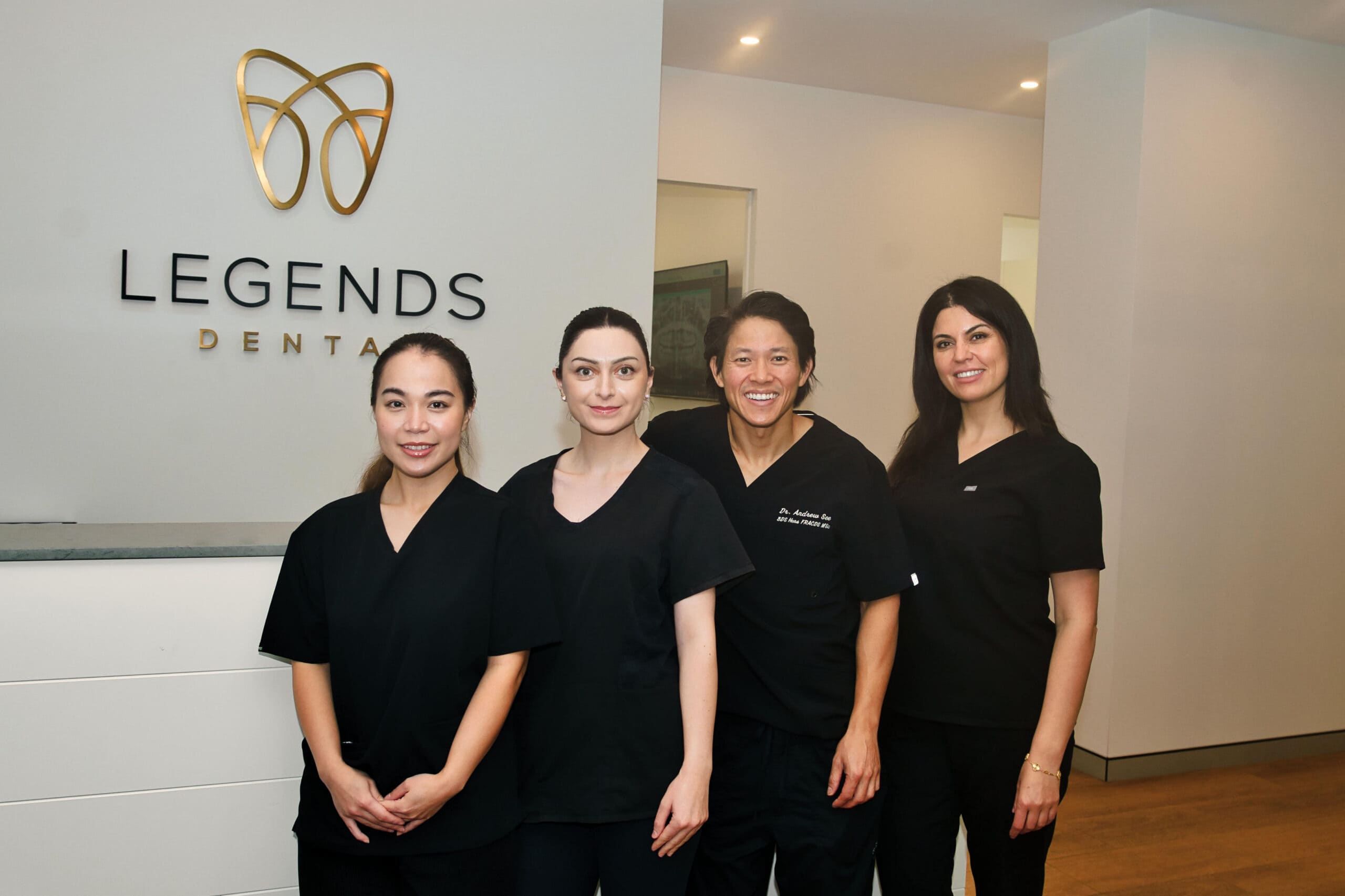 The Legends Dental team of dentists and staff standing together in front of the Legends Dental branded reception wall