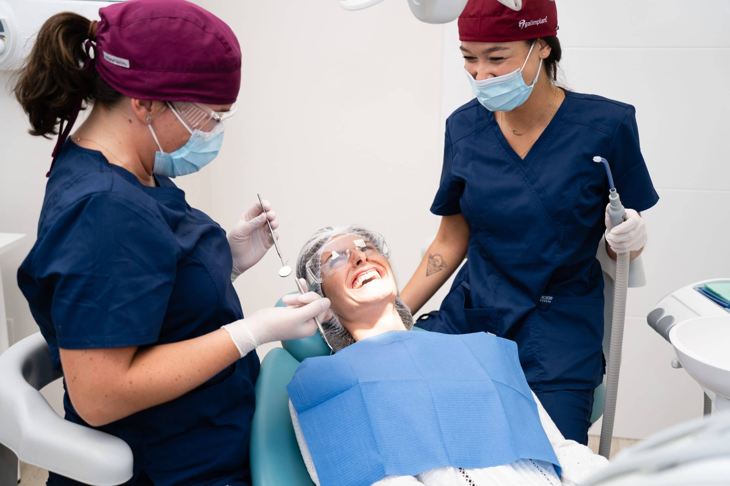 Dos profesionales dentales (odontólogas/higienistas) con una paciente sonriendo en el sillón de tratamiento.