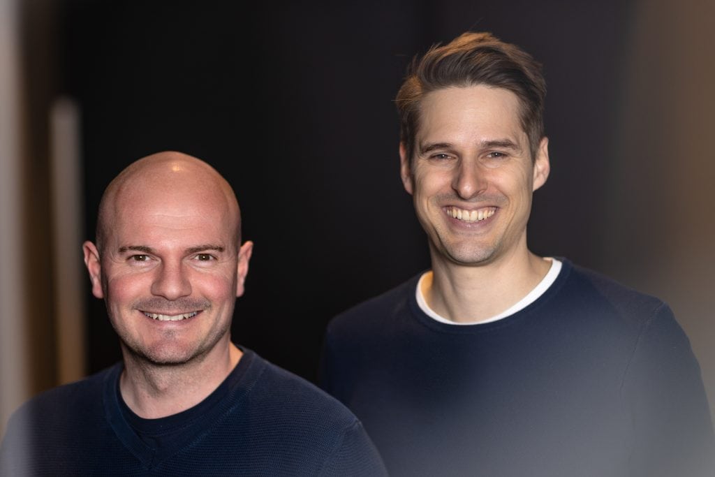 Zwei lachende Männer vor dunklem Hintergrund, professionelles Portrait.