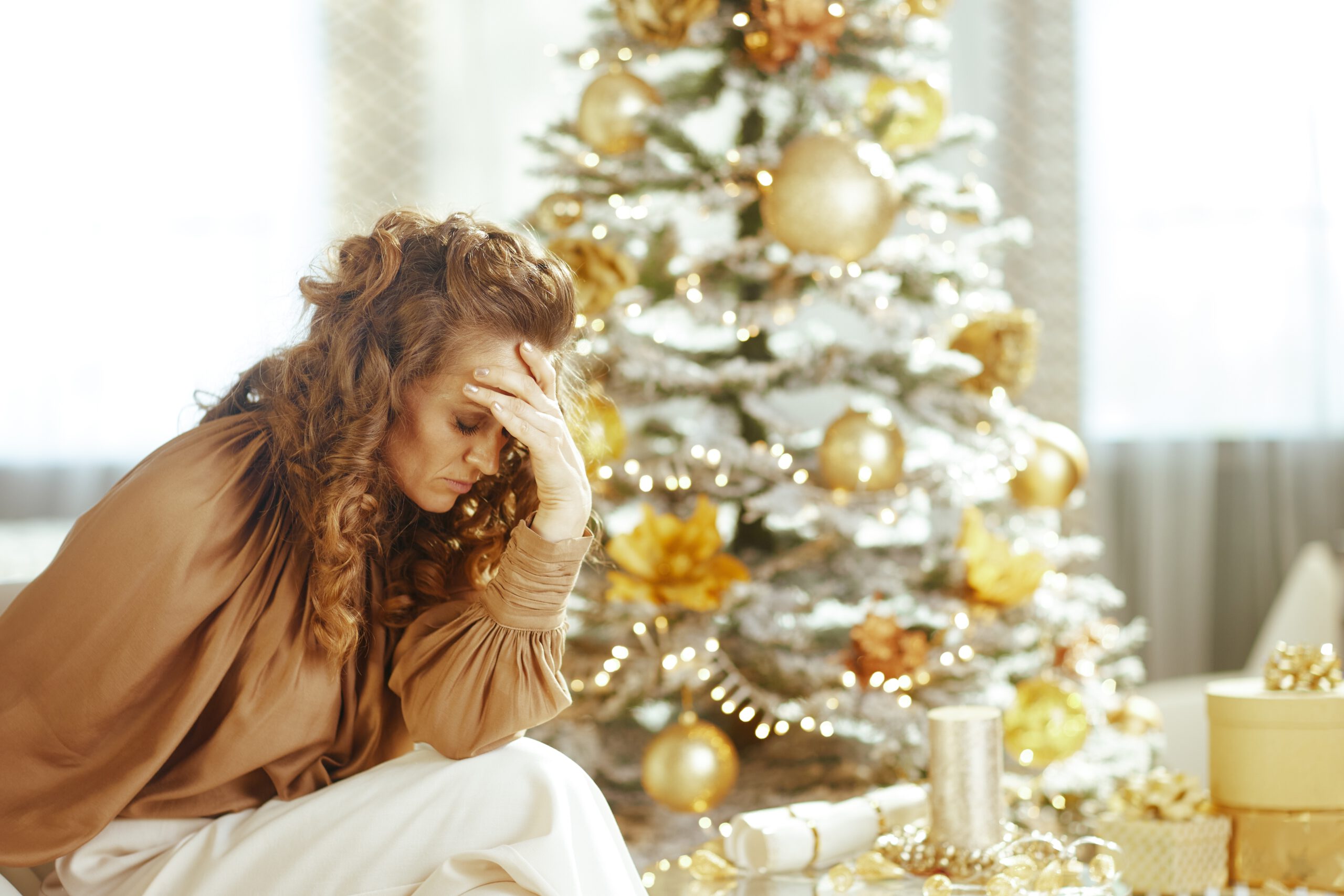 Gestresste junge Frau vor Weihnachtsbaum – Weihnachtsstress bewältigen in der Vorweihnachtszeit.