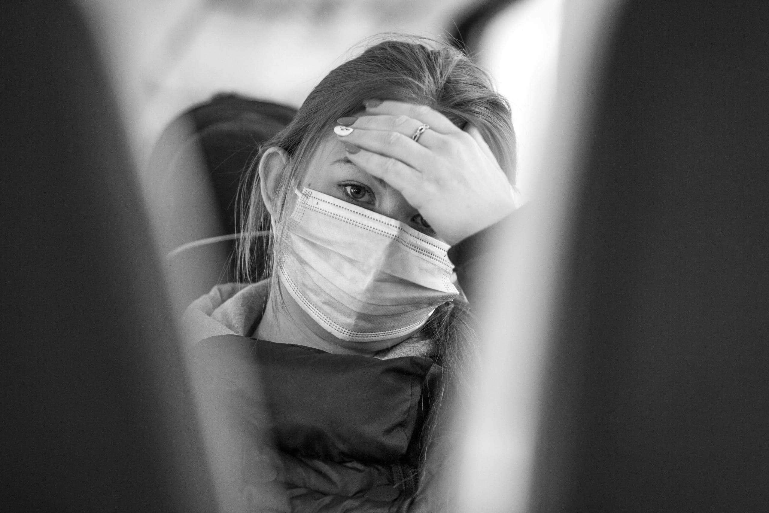 A woman wearing a face mask looks worried while traveling on public transport, emphasizing health concerns.