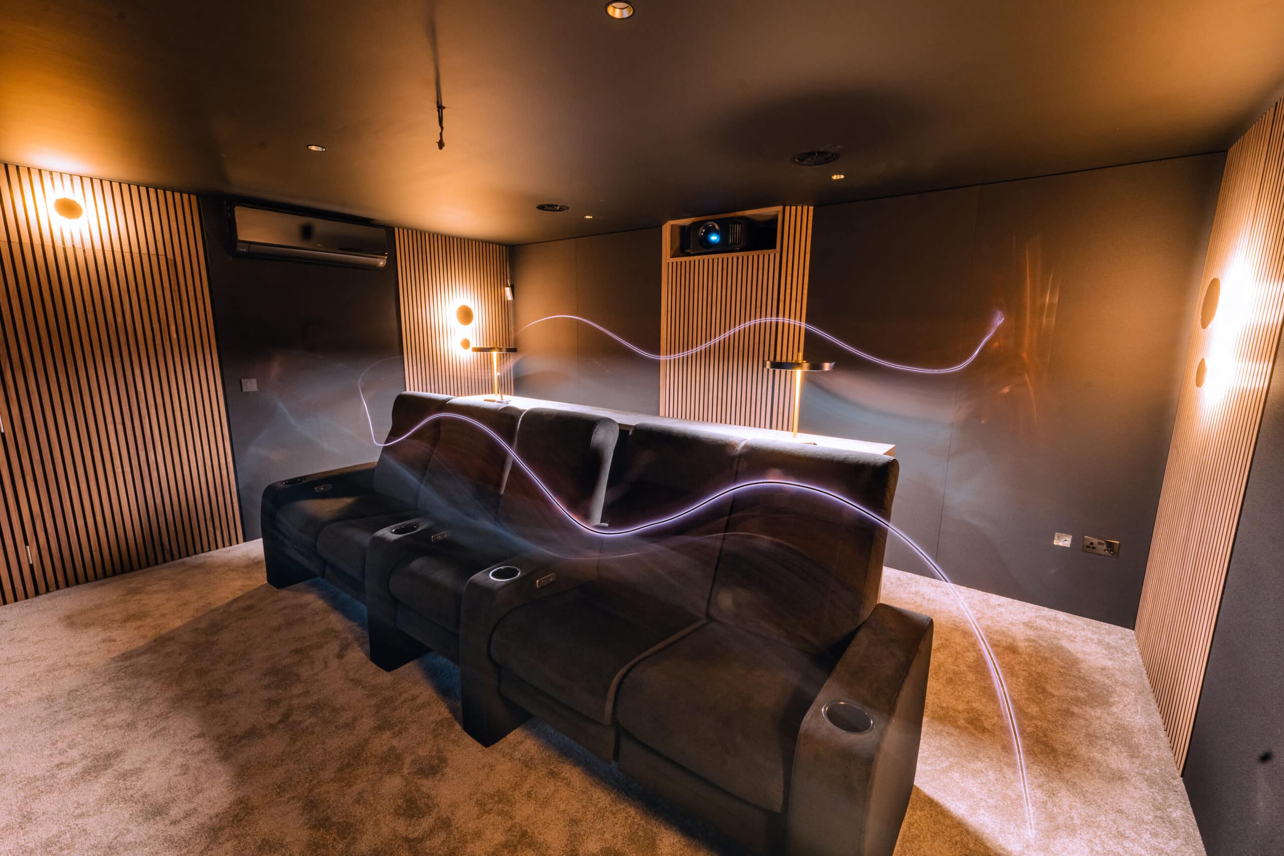 Garden room cinema with a dark leather recliner sofa, timber slat wall panels and wall lights
