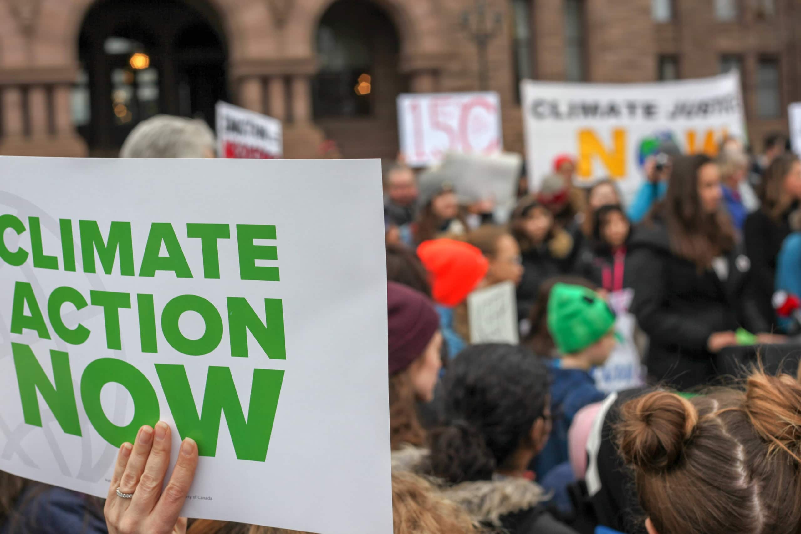 hand holding a sign reading Climate Action Now at a protest