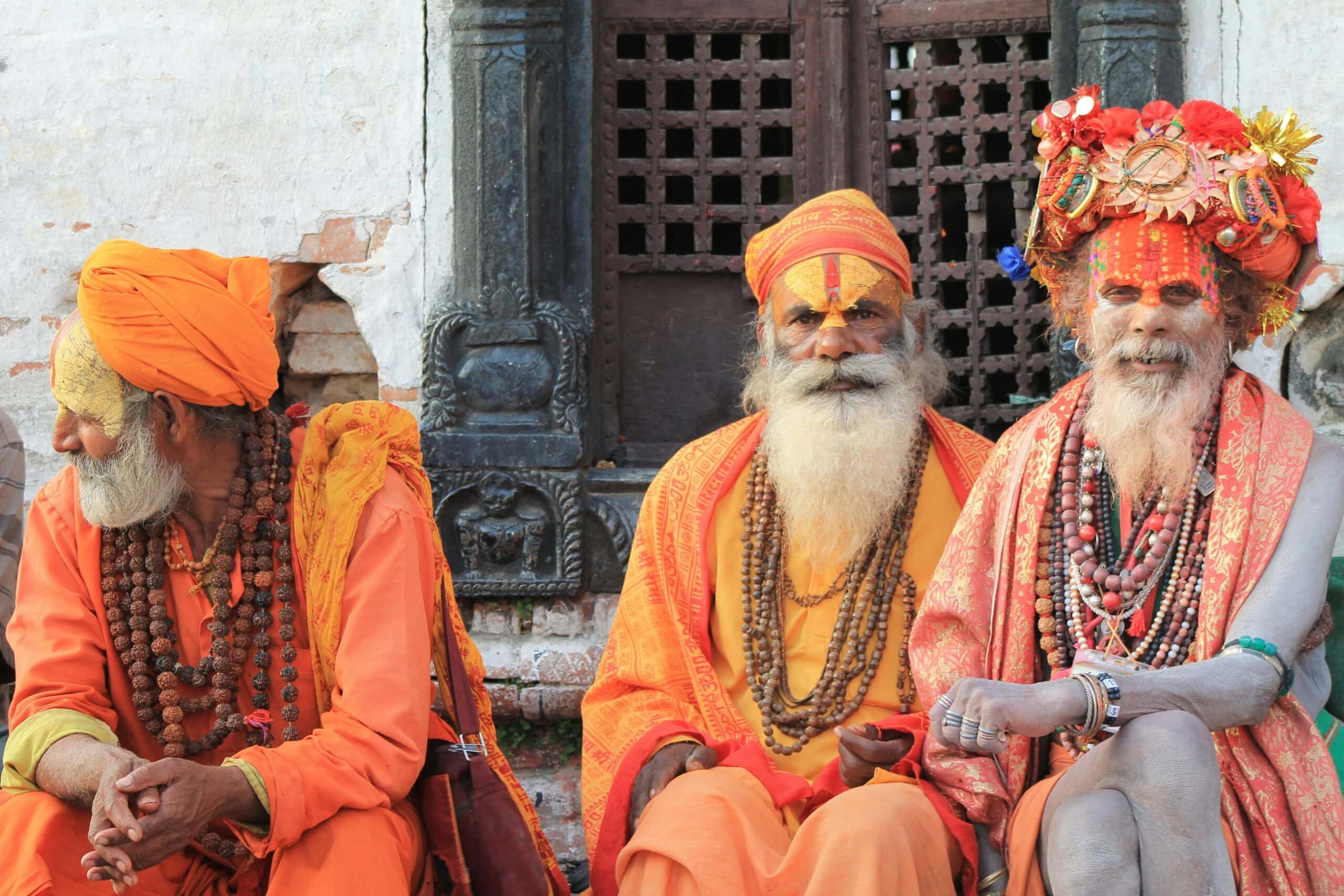 Three sadhus in orange robes with painted faces at Pashupatinath Temple, Kathmandu, Nepal.