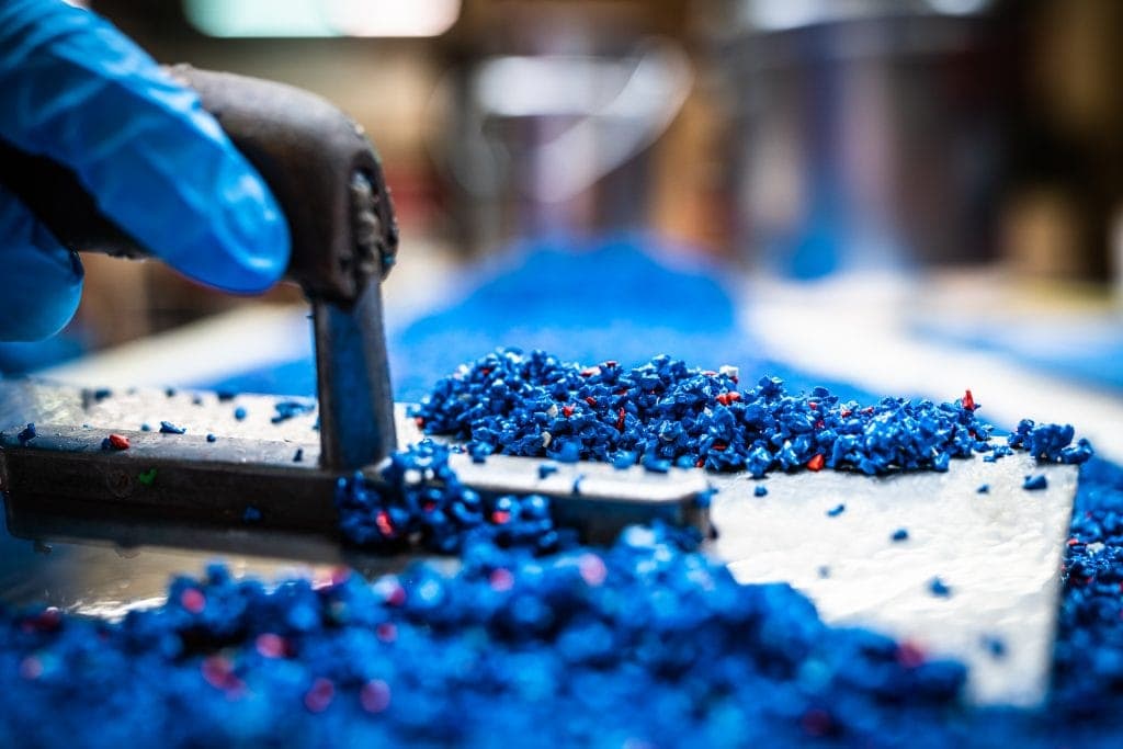 Hand, die blaue Perlen mit einer Zange auf einer Werkbank platziert.