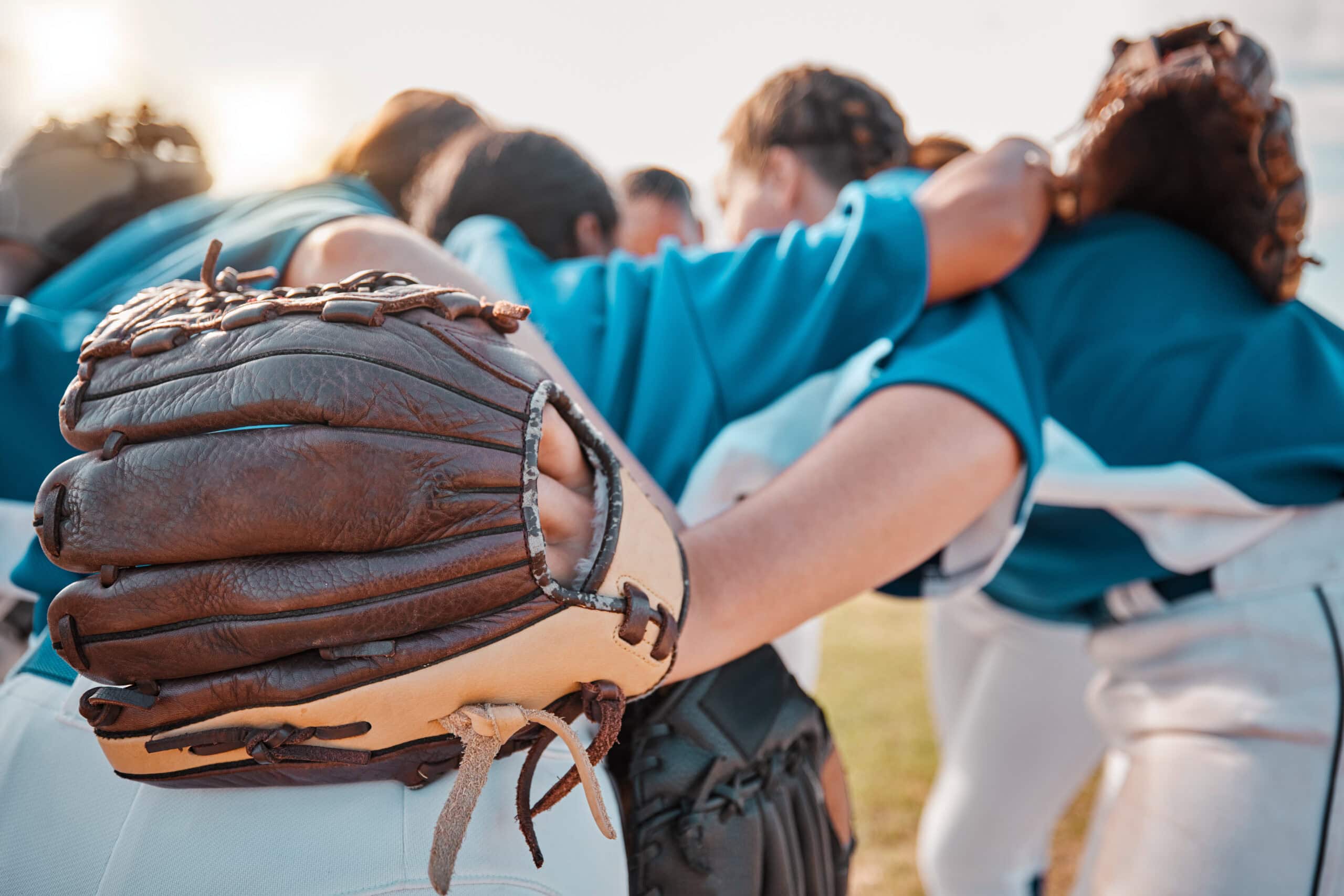 Group of female softball players huddled up with their gloves before a game.