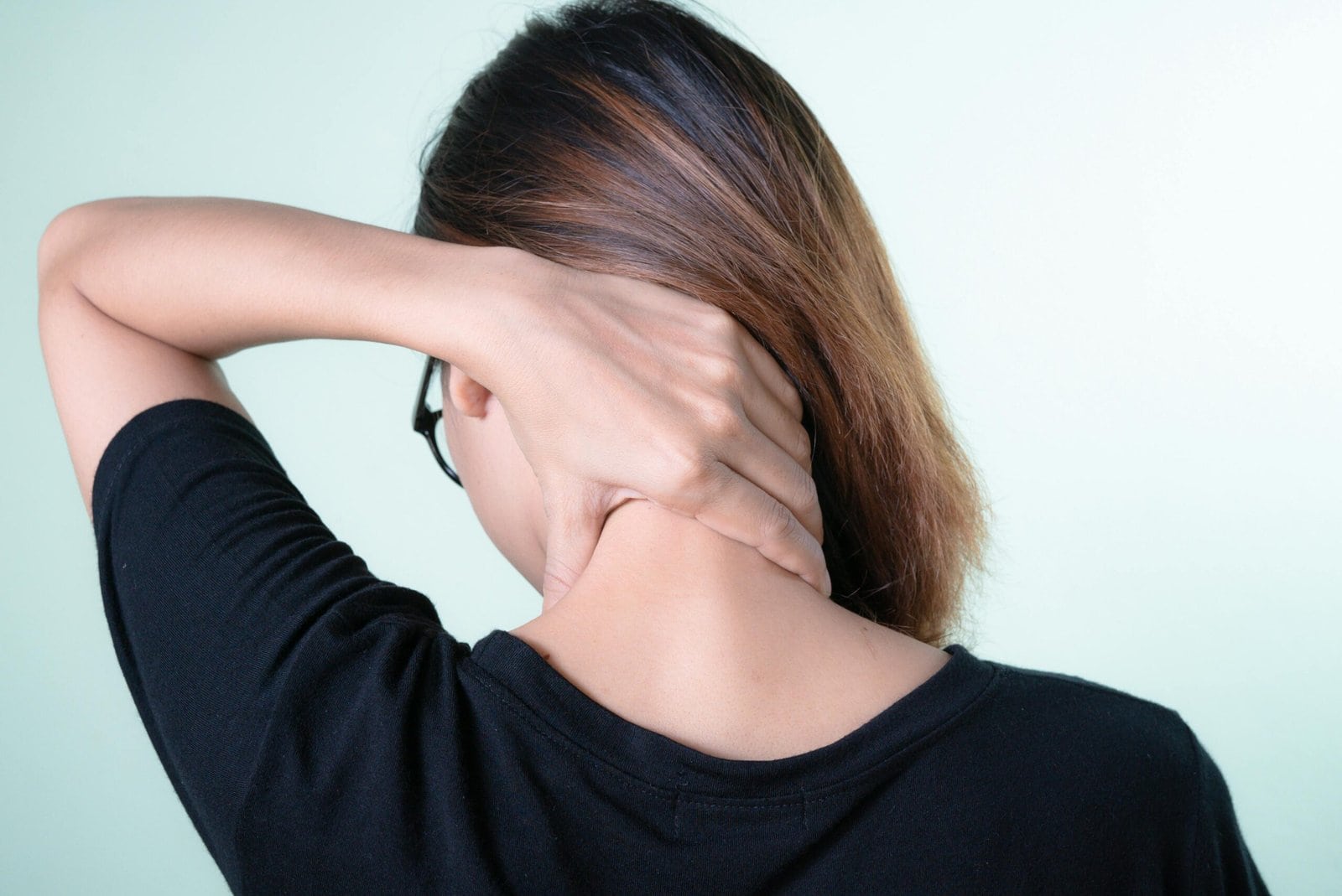 Rear view of a woman massaging her neck, depicting neck pain relief or self-care concepts.