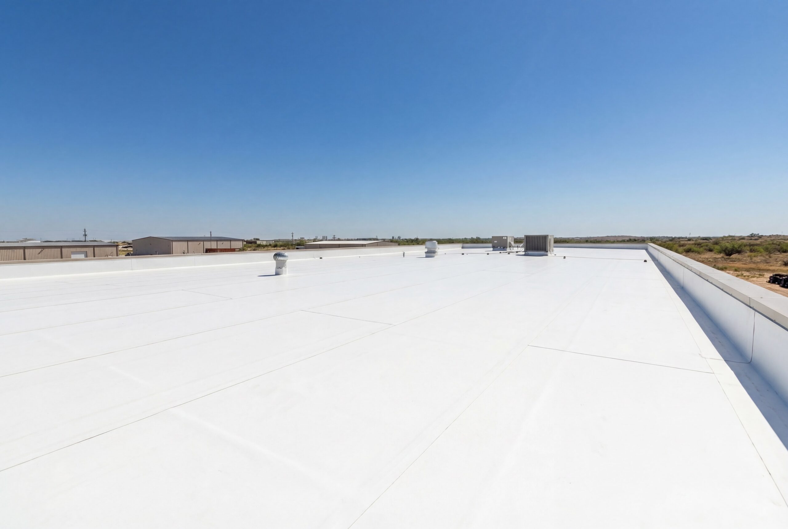 Flat white commercial TPO roof with rooftop vents under a clear blue sky