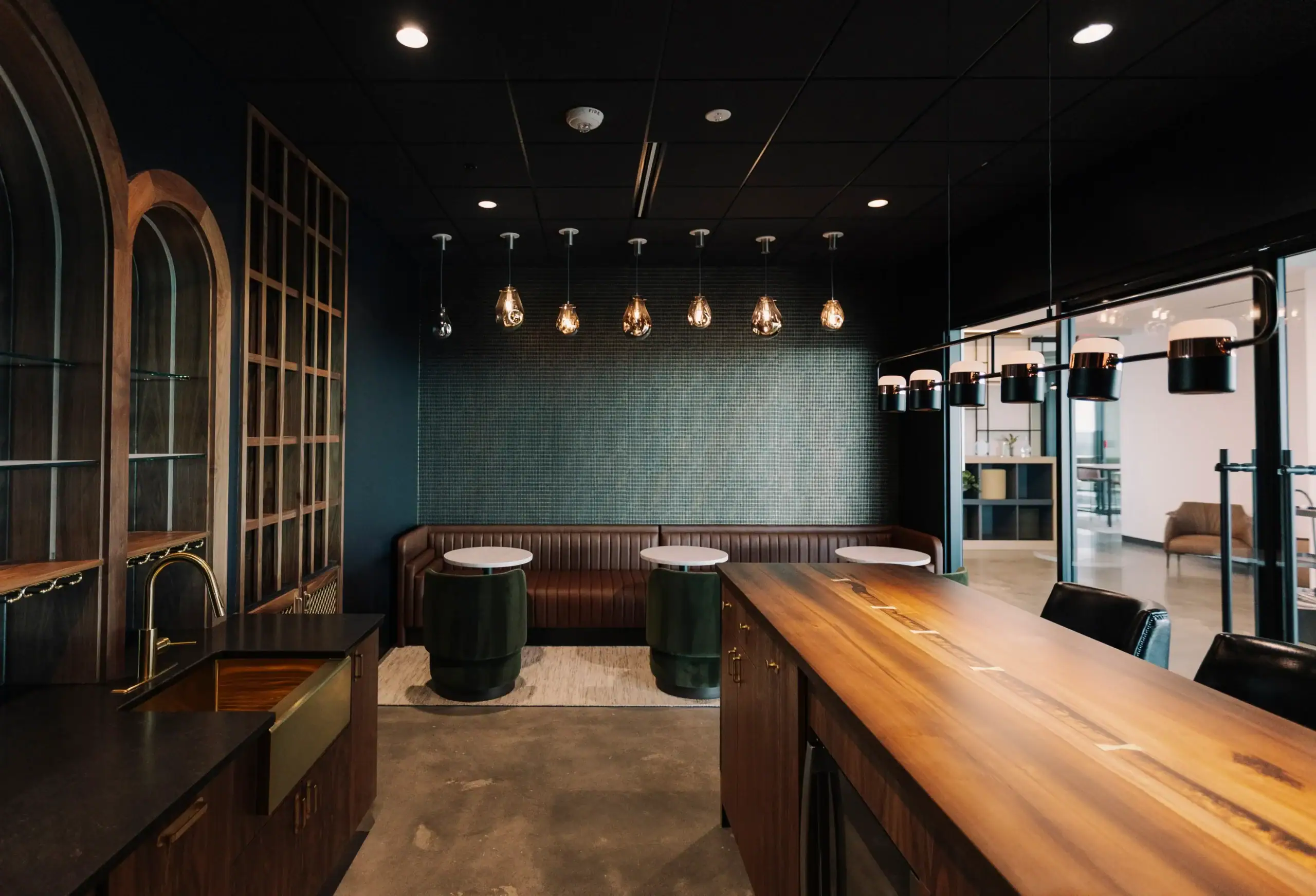 Modern private meeting lounge featuring a live-edge wood conference table, built-in wet bar, booth seating, and contemporary pendant lighting.