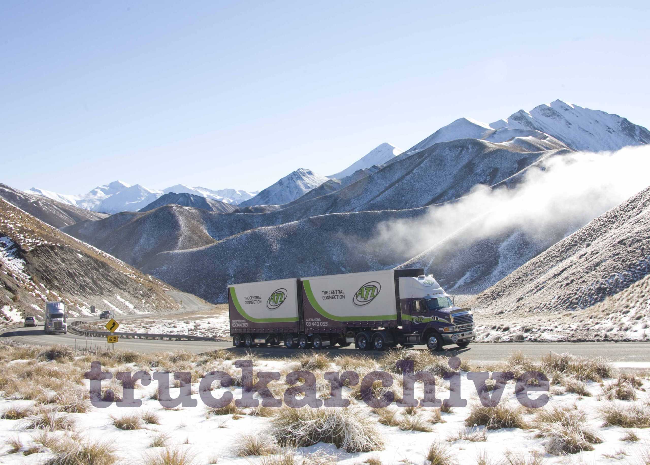 Heavy-duty truck transporting goods through snowy mountain landscape.