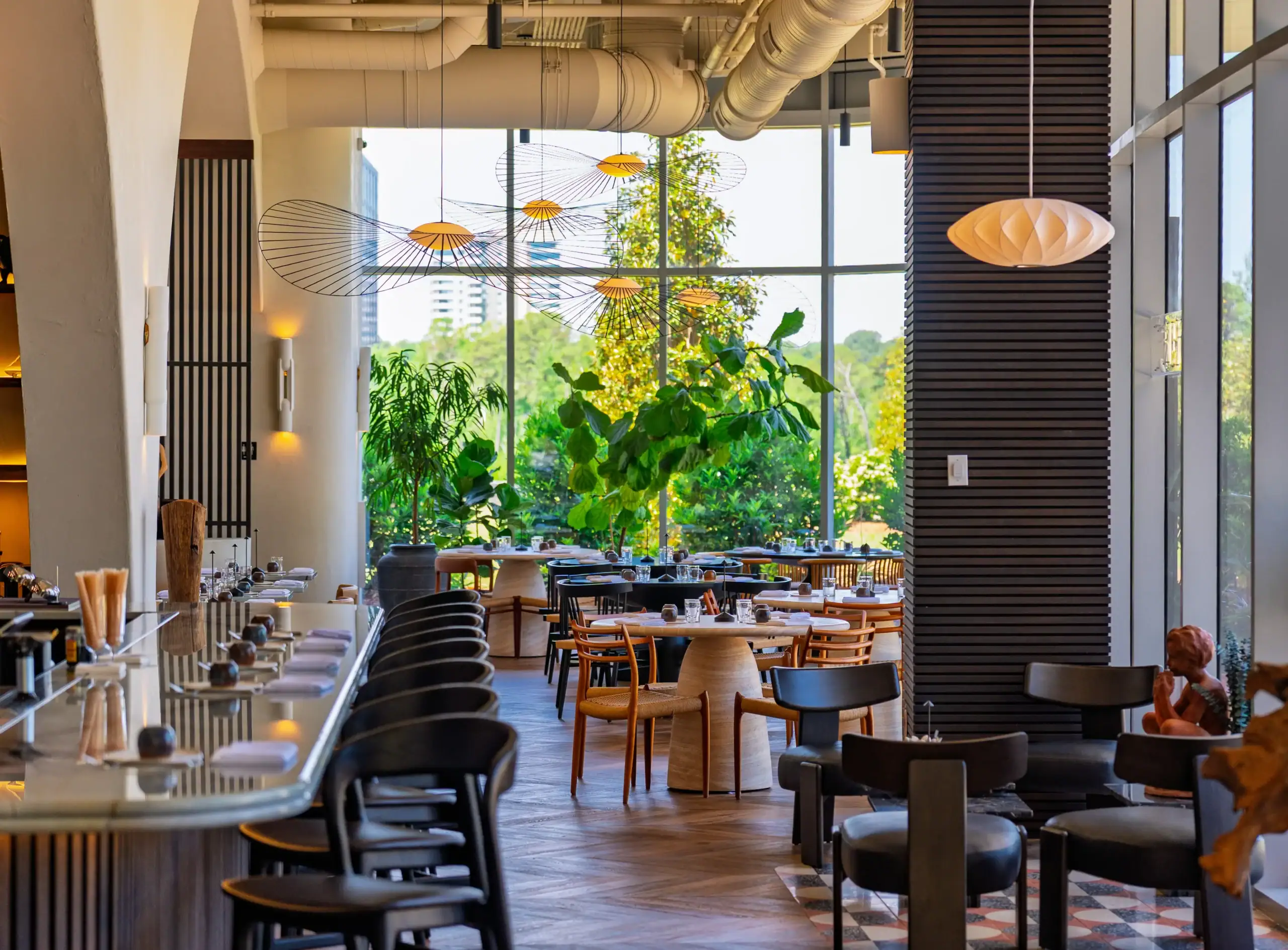 Interior view of Peregrine, a fine dining restaurant and bar in Raleigh featuring floor-to-ceiling windows, designer lighting, elegant seating, and lush garden views.