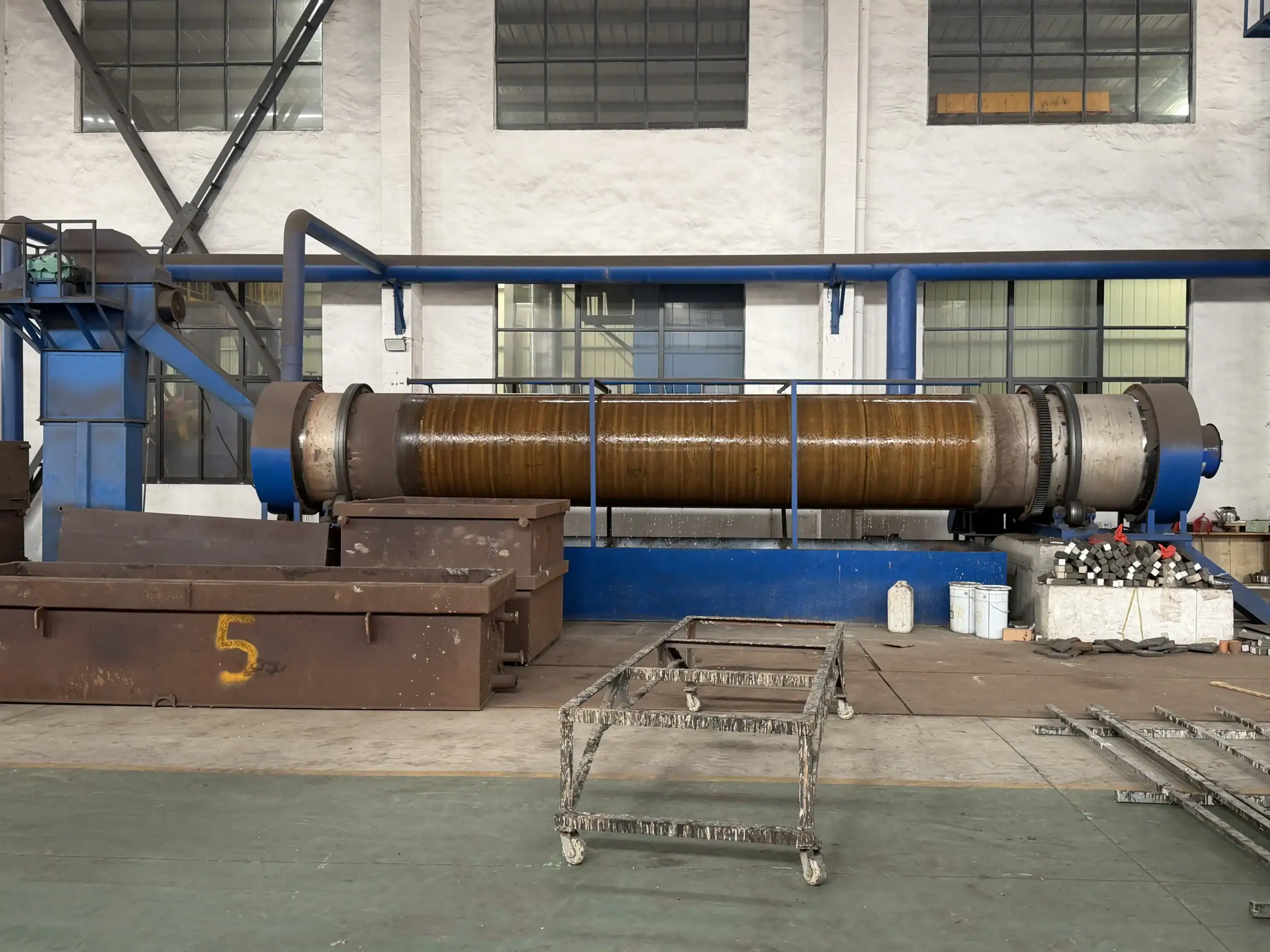 Long horizontal cylindrical production equipment supported on a blue steel frame