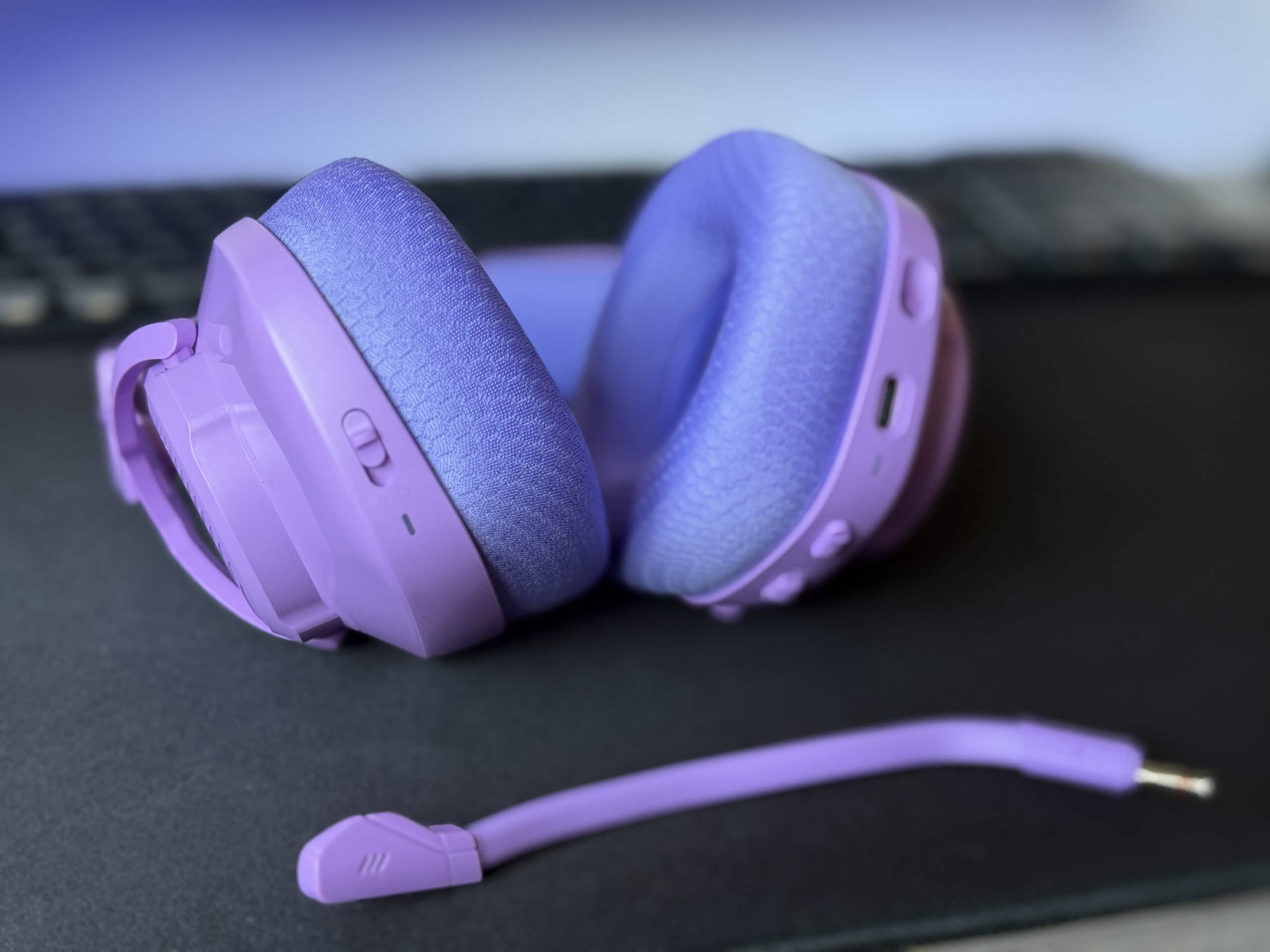 Purple JBL Quantum 360 headphones with a matching audio mic on a black surface.