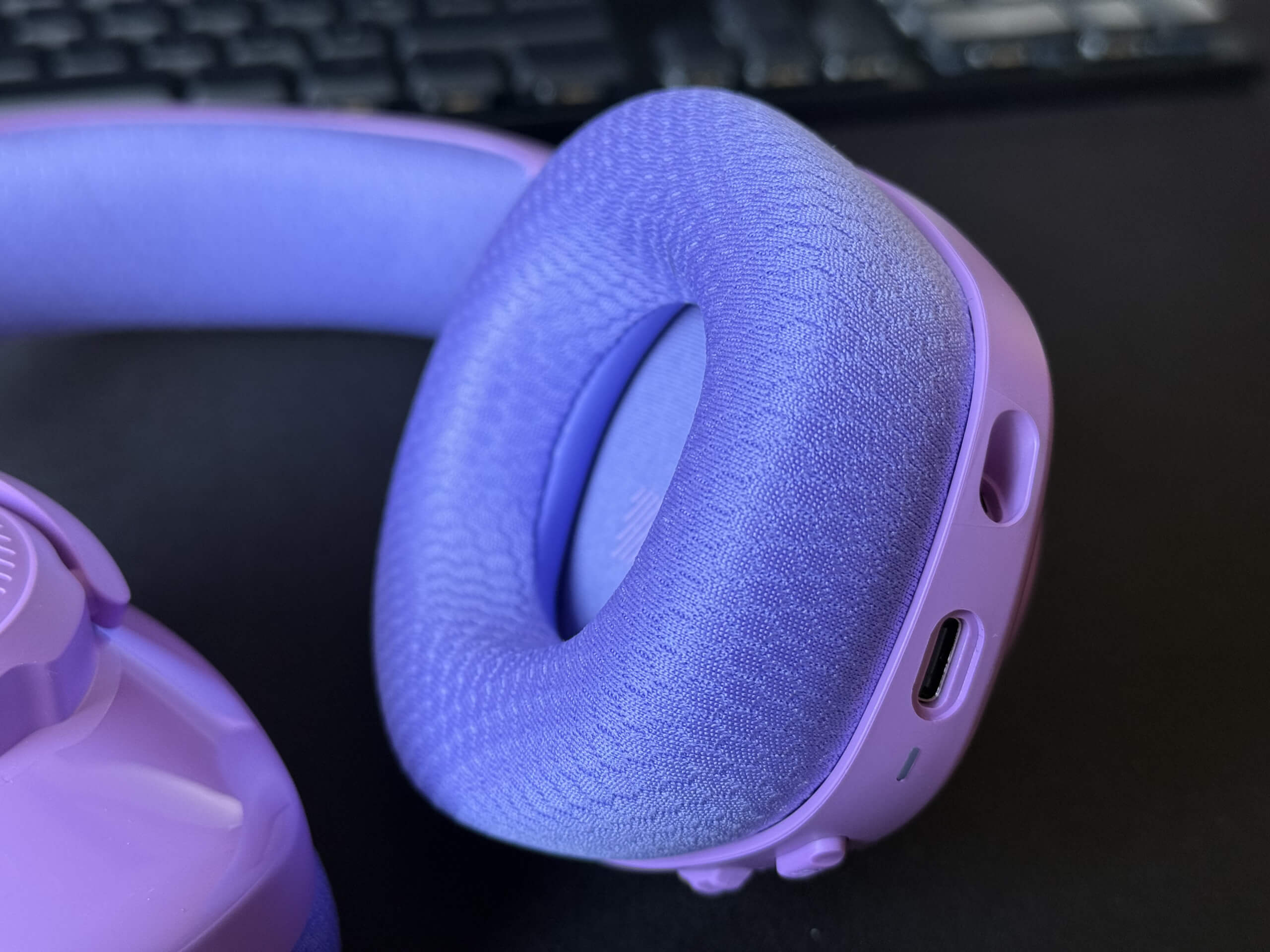 Close-up of JBL Quantum 360 purple headphone earcup with textured fabric and ports.