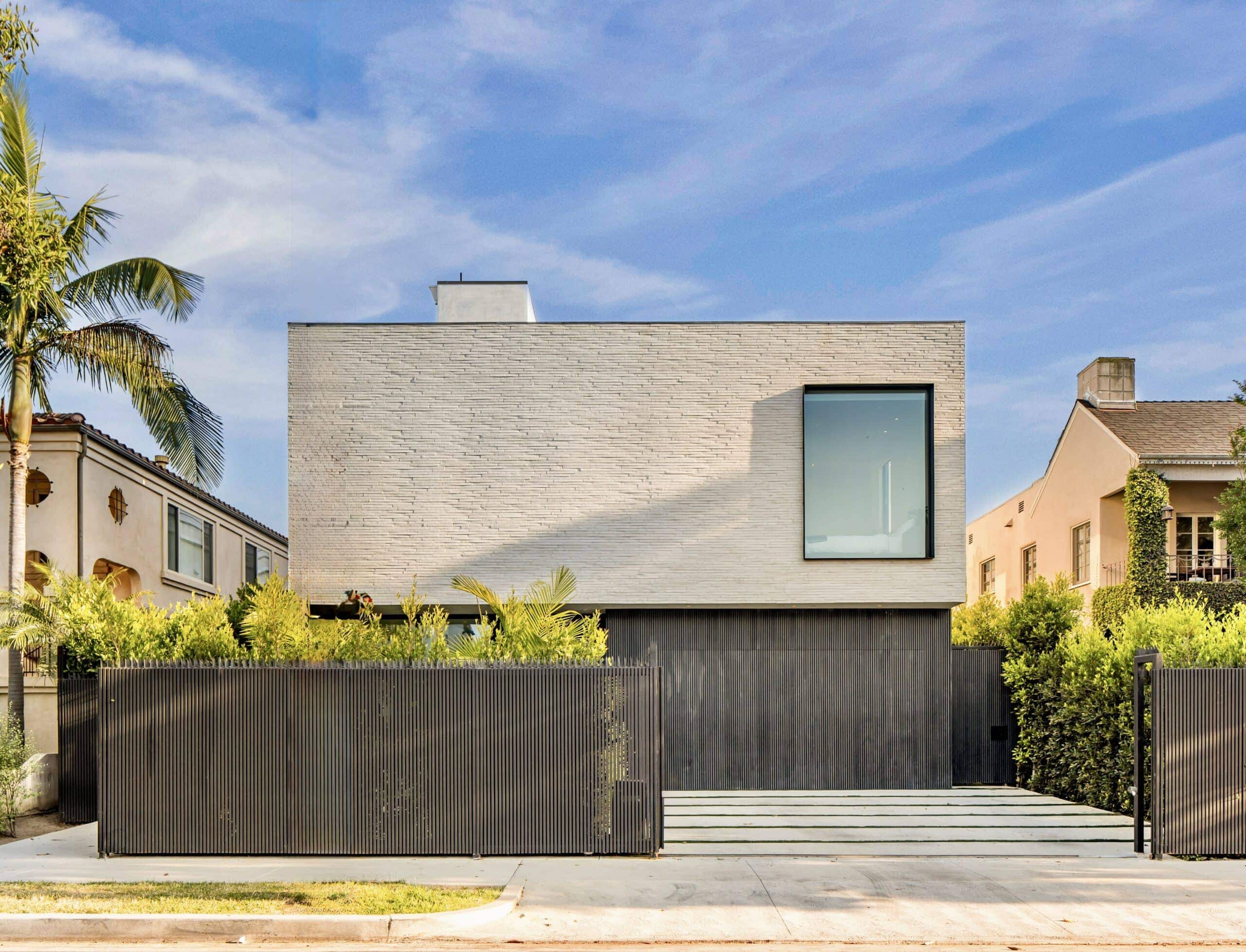 Front elevation of a Los Angeles modern single-family home by Bittoni Architects, featuring white plaster, vertical wood screening, and a large framed window.