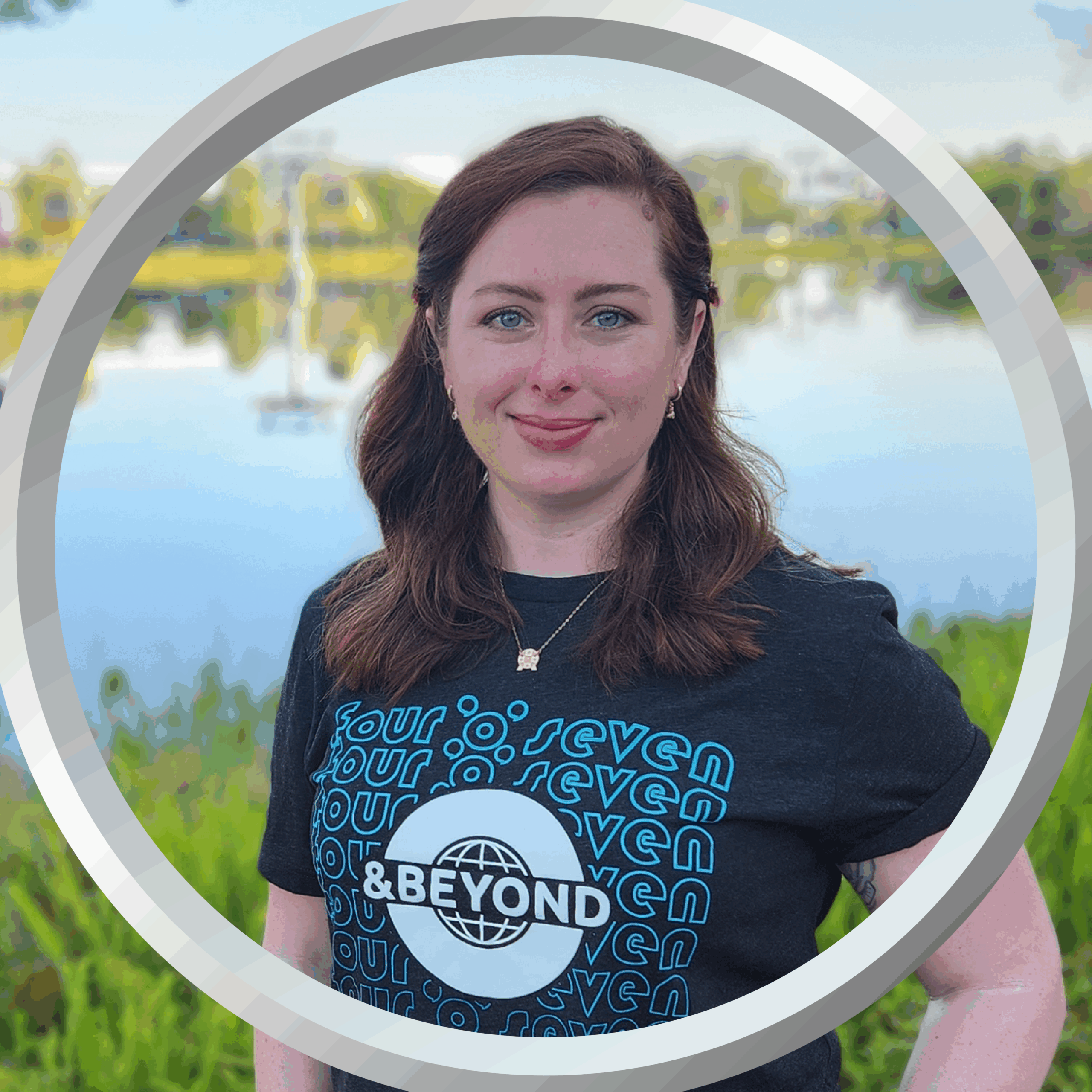 Relaxed woman wearing "407 and Beyond" t-shirt near a lake with boats and trees.