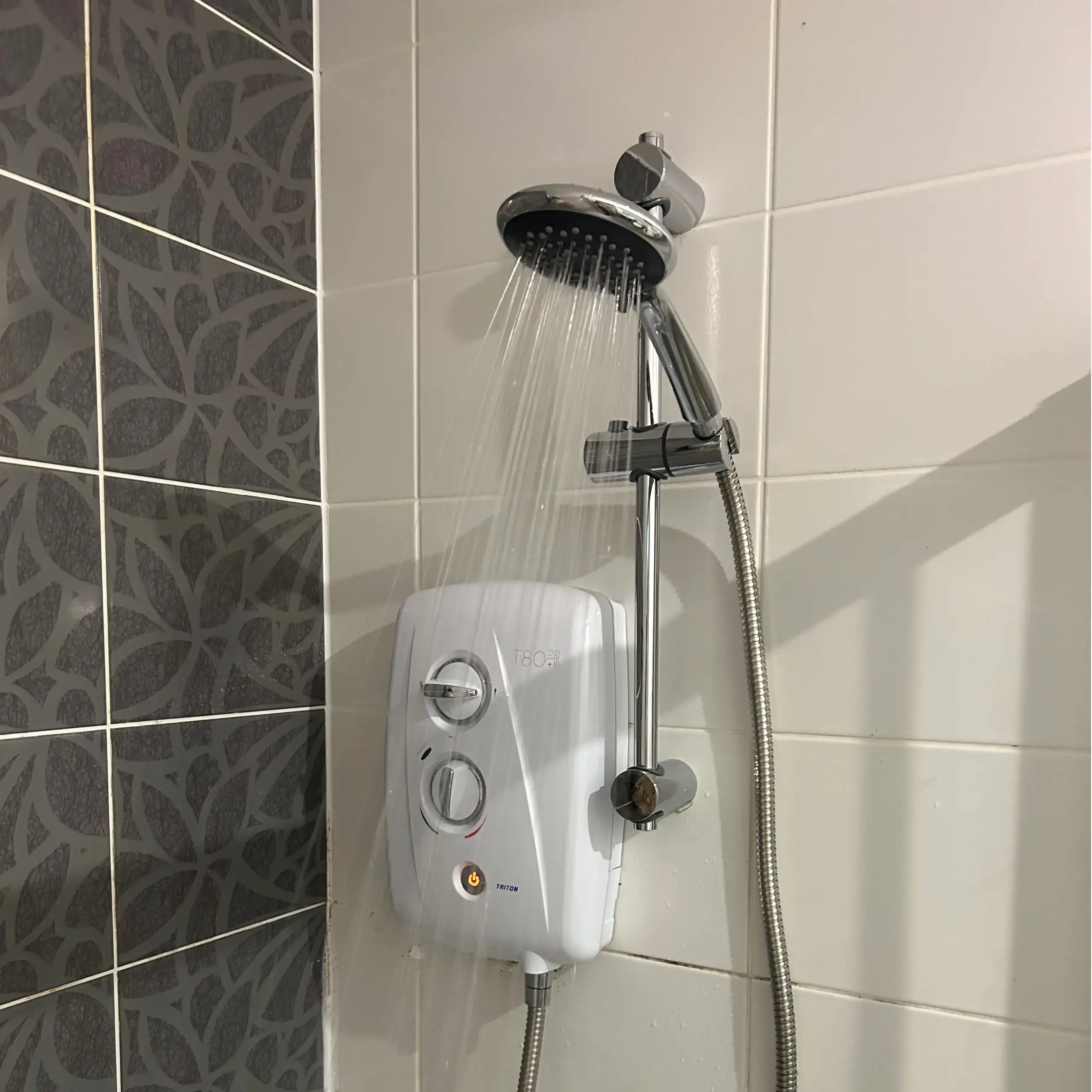 White Triton T80 electric shower unit running water, professionally supplied and fitted on a modern tiled bathroom wall by a local NB Gas And Plumbing plumber in Glasgow.
