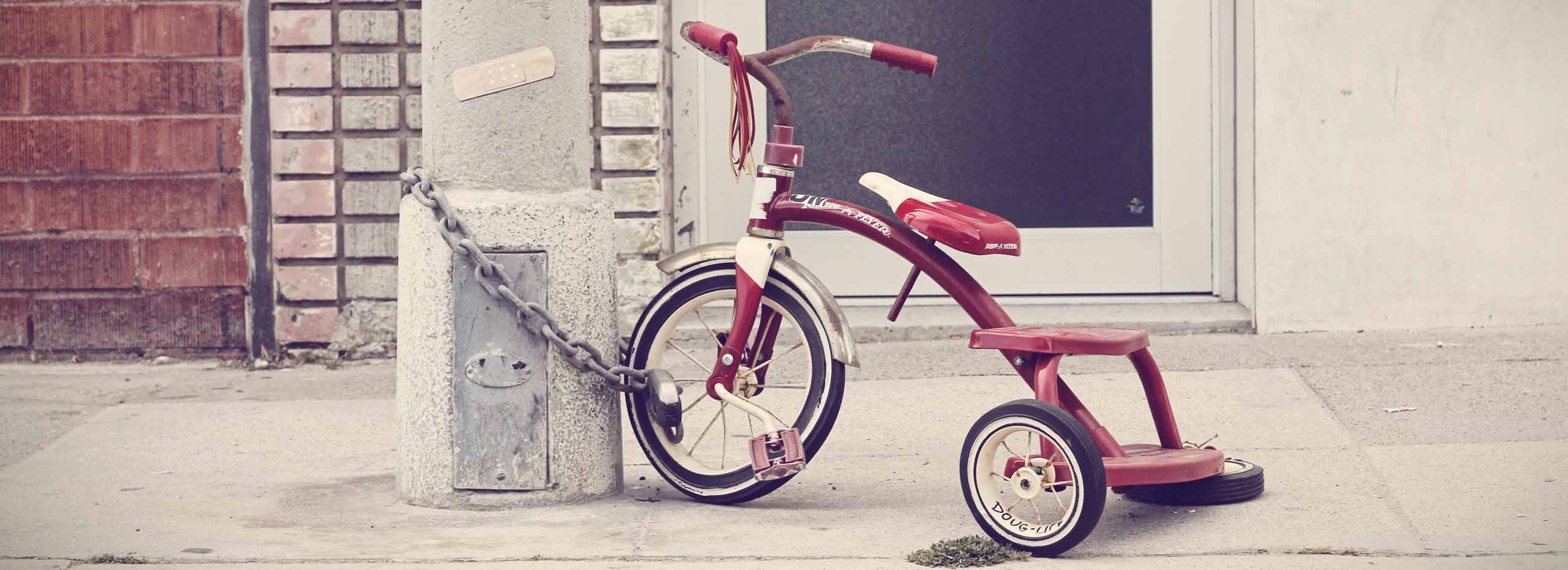 A child's tricycle is locked to a streetlamp in a city environment