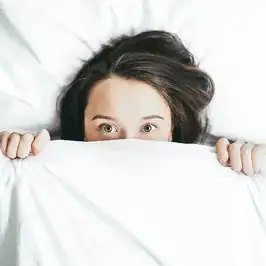 A woman covers her face with a bed sheet. Looking to start trauma therapy in Detroit, MI? Speak with a trauma therapist in Michigan today!