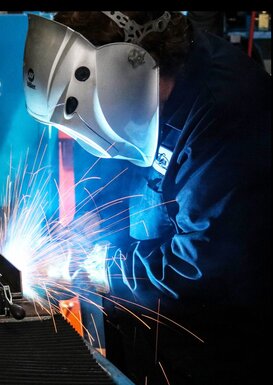 Side view of welder welding on a part with sparks flying