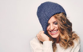 Smiling woman in chunky knit sweater and blue beanie, cozy background, representing dentistry.