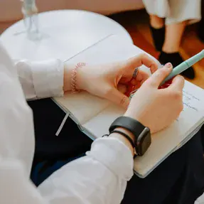 A close-up of hands holding a pen over a journal, symbolizing self-reflection and growth supported by IFS therapists in Michigan and IFS online therapy in Michigan.