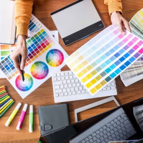 Image of female creative graphic designer working on color selection and drawing on graphics tablet at workplace with work tools and accessories, top view workspace.