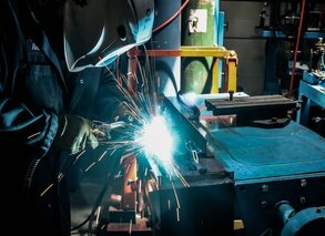 Welder MIG welding on part with sparks on a work table