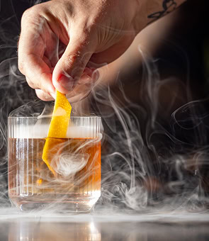 Smoke swirls around a whiskey cocktail as an orange twist is added in a Raleigh bar
