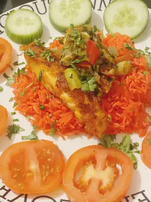 A beautifully plated dish of vibrant orange-red rice topped with a golden seared salmon fillet and sautéed vegetables. The salmon is garnished with chopped red pepper, leek, and parsley, and surrounded by fresh tomato and cucumber slices.
