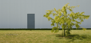 A modern industrial building with a closed grey metal door and a green tree in the foreground, representing Australian door regulations