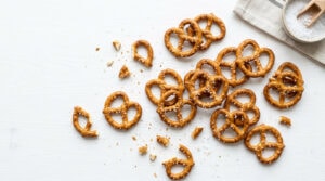 Hard salted pretzels scattered on a white surface with coarse salt and a bowl of sea salt.