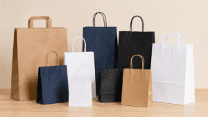 Assorted paper shopping bags in brown, white, navy, and black arranged on a wooden floor.