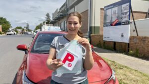 A successful student driver holding her official Service NSW practical test score sheet next to the training car.