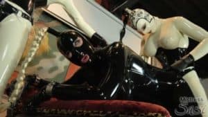 Dominatrix in latex with submissive in bondage gear.