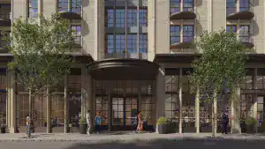 Modern mixed-use building with large glass storefronts and residential balconies, featuring beige brick facade and black window frames.
