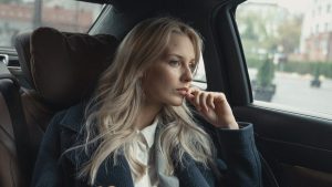 A millennial woman sitting in the back seat of a car.