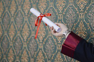 A graduate's hand holding a diploma with red ribbon, symbolizing achievement.