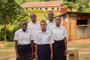 Group of African students in school uniforms standing outside a rural school building.