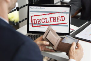 Man holding open his wallet in front of a laptop screen with a "DECLINED" stamped over a failed payment