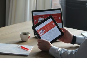 Business professional using a tablet and laptop with a hot drink, focusing on digital content review.