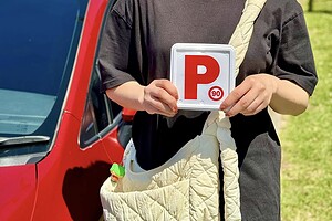 D-Tech Driver Training student smiling and holding her new NSW P-plates next to the D-Tech driving school car after passing her practical test in Grantham Farm.