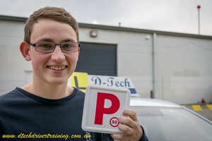 Student Brendan smiling while holding his red P-plate after passing his driving test at Blacktown Service NSW on his first attempt.