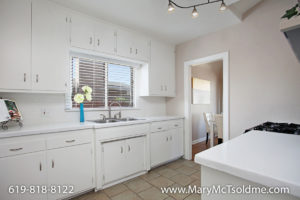 Clean white kitchen at 4433 Bancroft Street in Normal Heights featuring white cabinetry, a double sink with a window view, track lighting, and neutral tile flooring.