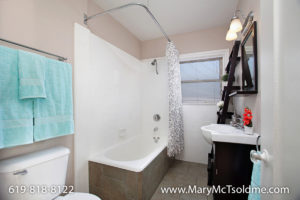 Bathroom at 4433 Bancroft Street in Normal Heights featuring a white pedestal sink, a bathtub with a white-and-grey floral shower curtain, and dark wood accents.
