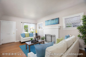 Sun-drenched living room at 4433 Bancroft Street in Normal Heights featuring a white brick fireplace, hardwood floors, a bright teal area rug, and modern white sofas with blue and lime green accents.